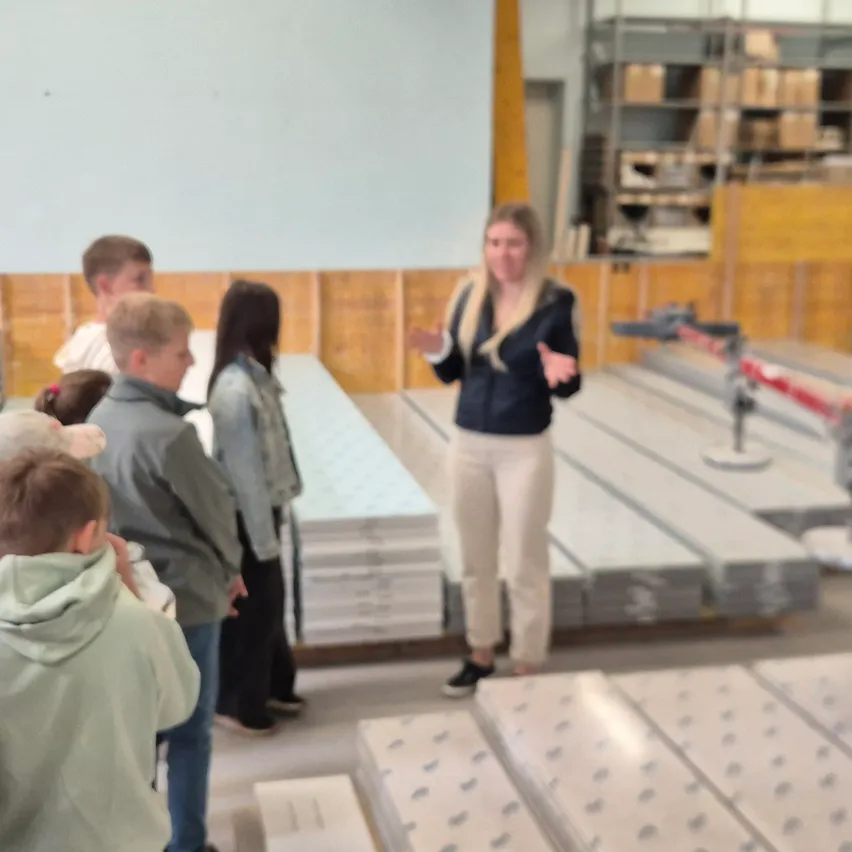 Eine Frau steht vor einer Gruppe von Kindern in einem Raum mit weißen Tafeln und Metallstrukturen und erklärt möglicherweise etwas.