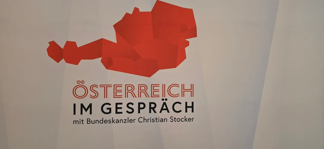 Ein Plakat mit einer roten abstrakten Form, die Österreich darstellt, mit dem Text 'OSTERREICH IM GESPRACH' und 'Bundeskanzler Christian Stocker' darunter.