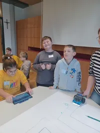Gruppe von Kindern und Erwachsenen, die in einem Klassenzimmer mit einem Roboter an einem Tisch arbeiten.