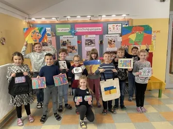 Eine Gruppe von Kindern posiert für ein Foto mit ihren Kunstwerken in einem Klassenzimmer. Sie halten ihre Stücke stolz.