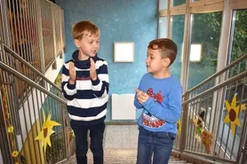 Zwei kleine Jungen stehen auf der Treppe. Einer trägt ein gestreiftes Shirt und der andere ein Spider-Man-Shirt. Sie unterhalten sich miteinander.