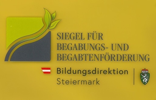 Ein gelbes Schild zeigt ein Blatt, ein Logo und deutschen Text 'SIEGEL FUR BEGABUNS-UND BEGABTENFORDERUNG', mit dem Logo der 'Bildungsdirektion' und 'Steiermark'.