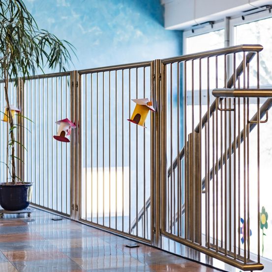 Ein Raum mit blauer Wand und weißer Decke hat ein glänzendes Metallgeländer und zwei Vogelhausdekorationen. Links steht ein Topf mit einer Pflanze.