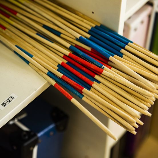 Eine Nahaufnahme mehrerer hölzerner Stäbe mit roten, blauen und gelben Bändern, die auf einem weißen Regal aufbewahrt werden, mit einem Etikett 'D-U1' auf der linken Seite sichtbar.