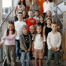 Eine Gruppe von Kindern und Erwachsenen steht auf einer Treppe, lächelt und posiert für ein Foto. Dahinter stehen einige Erwachsene auf der oberen Treppe.