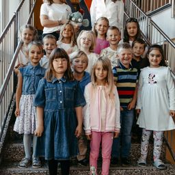 Eine Gruppe von Kindern und zwei Erwachsenen steht auf einer Treppe und lächelt für ein Foto. Ein Kind hält ein Kuscheltier.