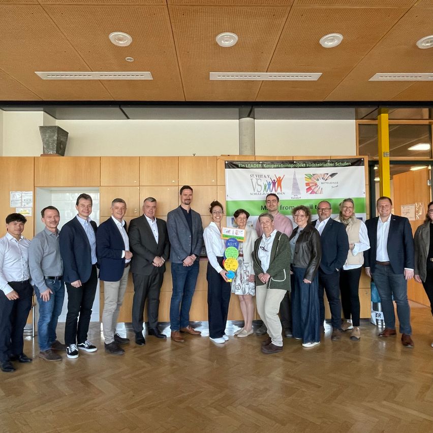 Gruppe von Fachleuten und Studenten posiert für ein Foto in einem Konferenzraum mit einem Banner dahinter.