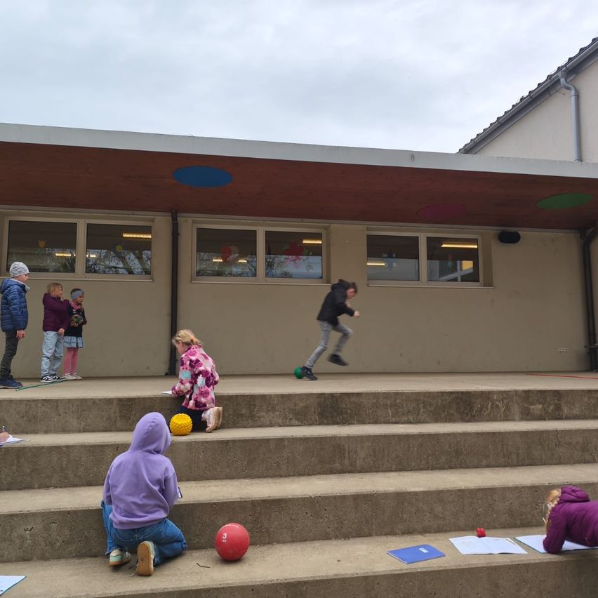 Kinder auf einer Schultreppe spielen Ballspiele. Ein Junge springt mit einem Ball in der Hand. Zwei Kinder schreiben auf Papier.