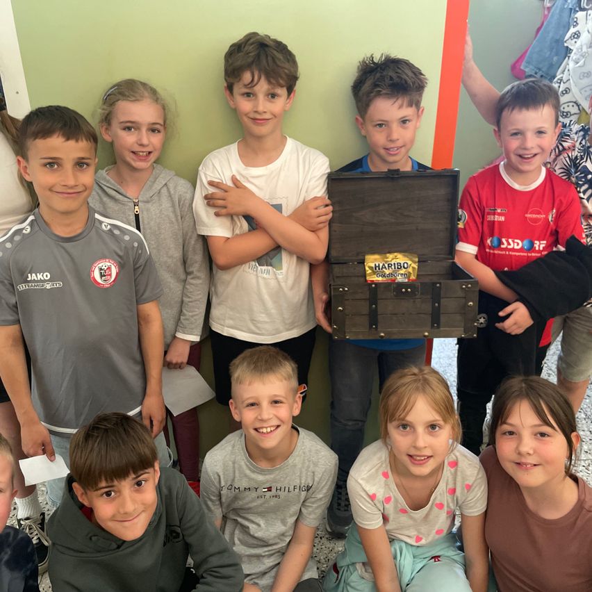 Eine Gruppe von Kindern steht zusammen mit einer Holztruhe in der Mitte. Sie alle haben fröhliche Gesichter und posieren für ein Foto.
