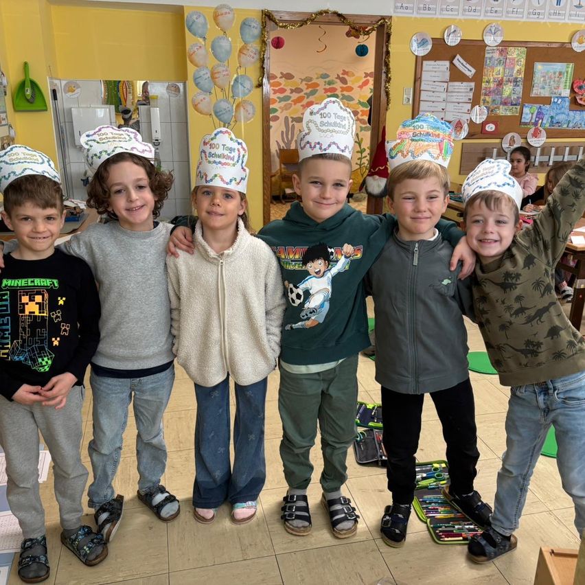 Fünf Jungen in einem Klassenzimmer, alle mit Papier-Kochmützen, stehen in einer Reihe. Ein Junge hat ein Minecraft-Shirt an.