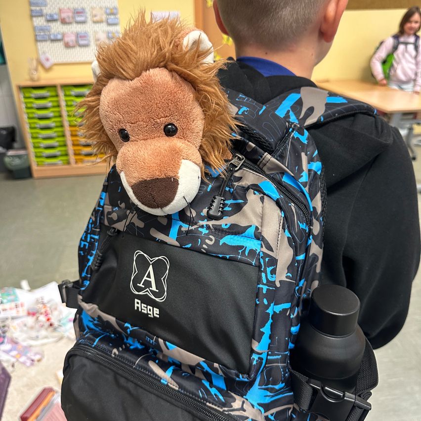 Ein junger Junge trägt einen Tarnrucksack mit einem Löwen-Plüschtier darauf.