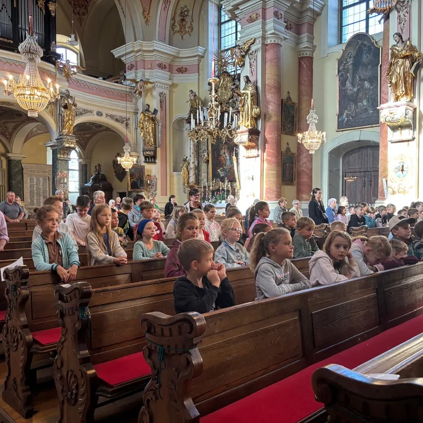 Eine Gruppe von Kindern und Erwachsenen sitzt in Kirchenbänken, einige schauen nach unten, andere nach oben.