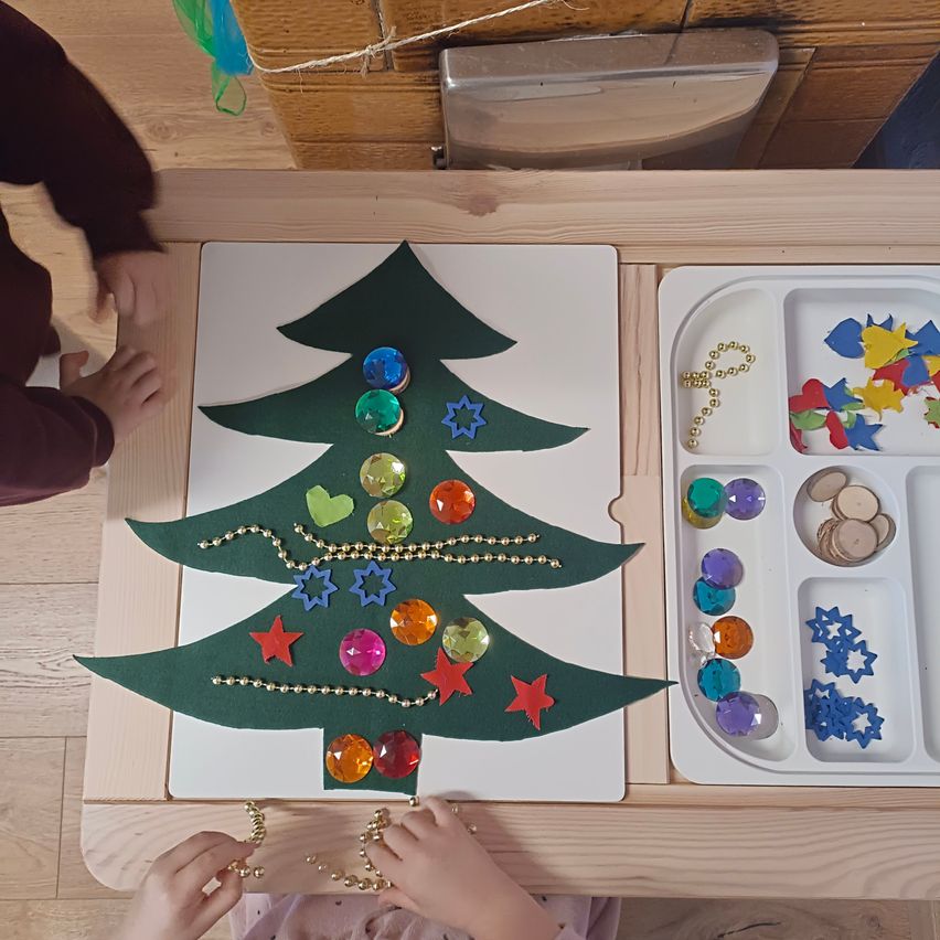 Ein Weihnachtsbaum-Dekorationsprojekt auf einem Holztisch, geschmückt mit bunten Perlen und Sternen. Der Tisch enthält eine Schale mit zusätzlichen Perlen und Dekorationen.