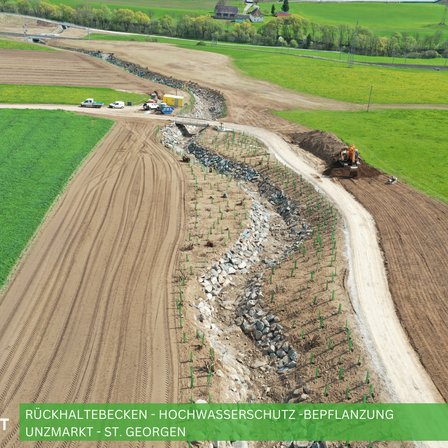 Luftaufnahme einer Baustelle in einem ländlichen Gebiet mit Fahrzeugen, Maschinen und einer Brücke. Grüne und braune Felder sind sichtbar.