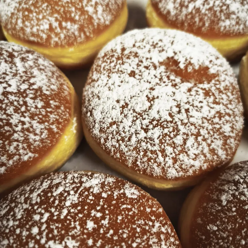 Ein Nahaufnahme von mehreren frisch glasierten Donuts, die mit Puderzucker bedeckt sind. Die Donuts haben eine reichhaltige, braune Glasur und sind in einer Reihe angeordnet.