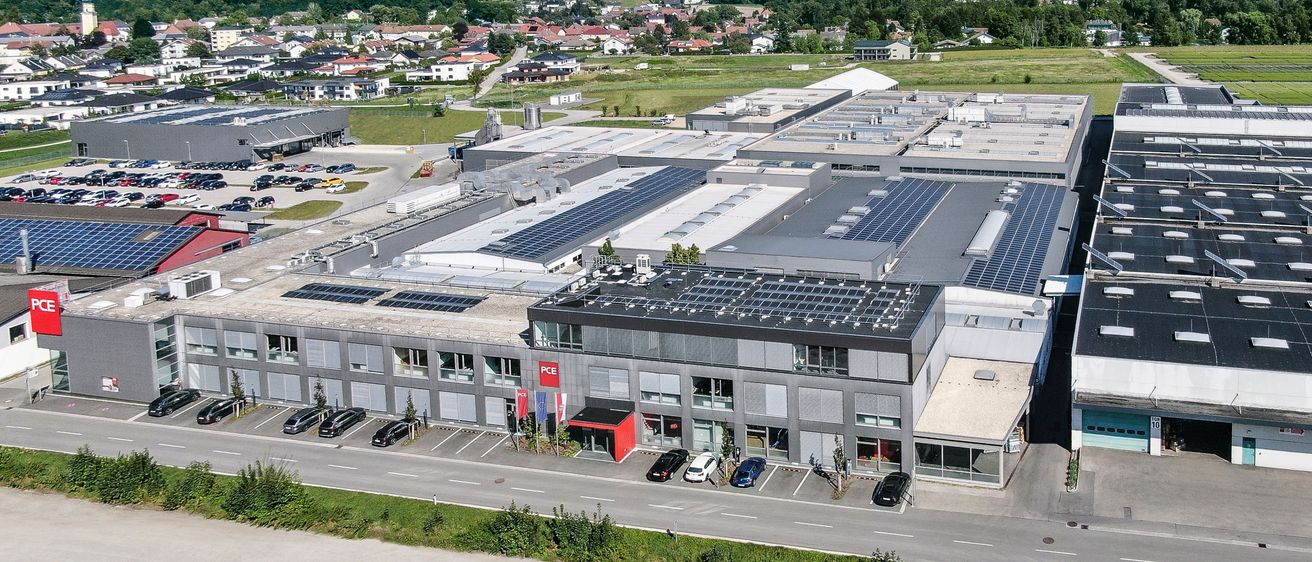 Luftaufnahme eines großen Industriegebäudes mit Solarpanelen auf dem Dach. Viele Autos sind vor dem Gebäude geparkt.