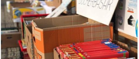 Stapel von Kartons mit Büchern, ein Schild oben drauf sagt 'BUCHERBASAR'. Die Kartons sind offen, und einige Bücher sind aufeinandergestapelt. Ein roter Kasten ist links.