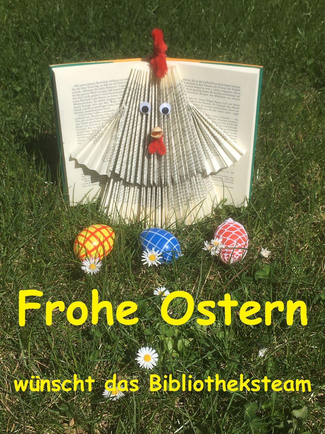 Ein offenes Buch mit einer gefertigten Papier-Hühnerfigur steht auf Gras. Drei bunte Ostereier liegen in der Nähe, geschmückt mit weißen Gänseblümchen. Die Worte 'Frohe Ostern' erscheinen in gelbem Text.