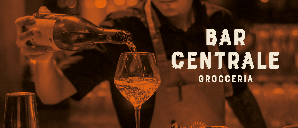 Ein Barkeeper schenkt Wein in ein Glas in der Bar Central Grocer. Der Hintergrund ist schwach beleuchtet und schafft eine gemütliche Atmosphäre.