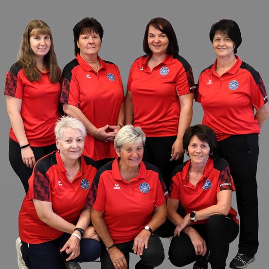 Sieben Frauen in roten und schwarzen Sportuniformen mit Logo auf der Brust, lächelnd und posieren für ein Foto.