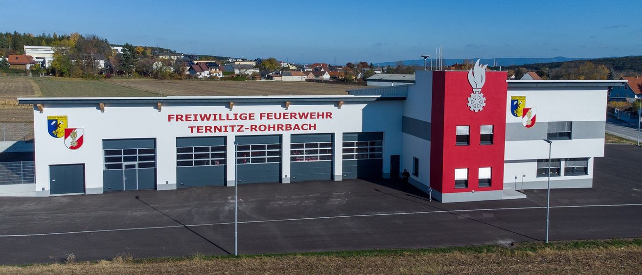 Eine Luftaufnahme eines Feuerwehrhauses mit rot-weißem Farbschema, das die Worte 'Freiwillige Feuerwehr Ternitz-Rohrbach' trägt. Mehrere Garagen sind zu sehen.