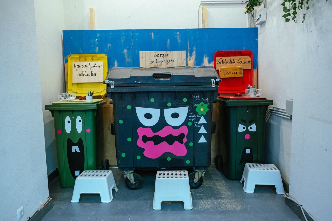 Vier bemalte Behälter sind mit Comic-Gesichtern ausgestellt. Einer hat ein Monstergesicht, ein anderer ein verärgertes Gesicht und der dritte ein lächelndes Gesicht. Jeder Behälter hat ein Schild mit seinem Zweck.