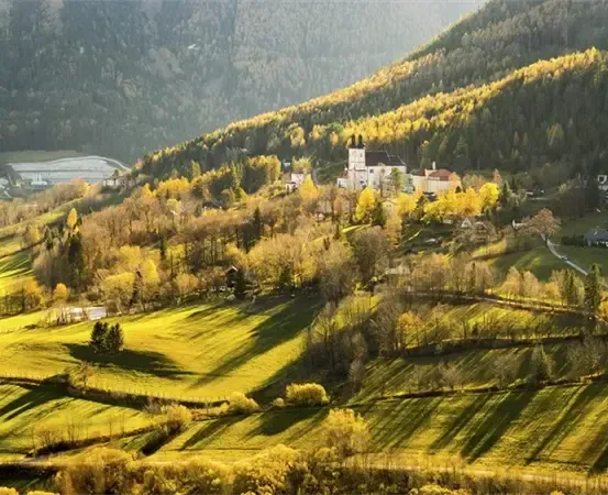 Eine landschaftliche Ansicht eines Hügels mit einem großen Gebäude, umgeben von grünen Feldern und Bäumen mit Bergen im Hintergrund.