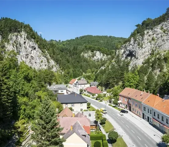 Eine kleine Stadt eingebettet zwischen Bergen und Bäumen, mit einer Straße und einigen Gebäuden. Die Stadt ist von üppigem Grün umgeben und hat einen klaren blauen Himmel.