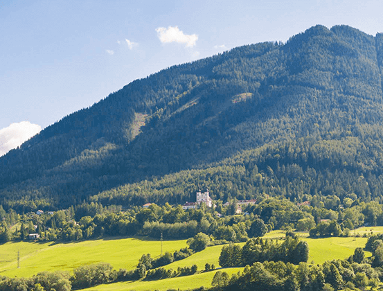Ein Berg mit üppigem Grün und einem weißen Gebäude unter einem klaren Himmel mit weißen Wolken.