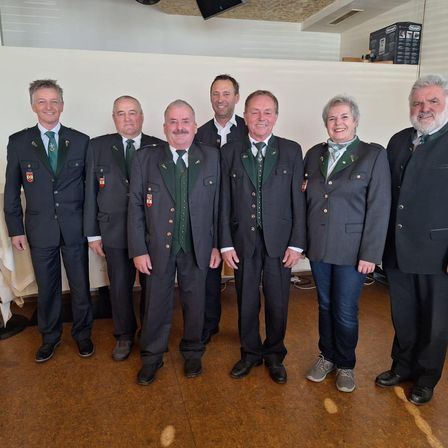 Eine Gruppe von Personen in formeller Kleidung mit grünen Westen und Abzeichen steht zusammen in einem Raum.