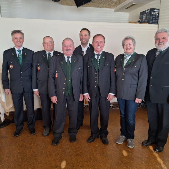 Eine Gruppe von Personen in formeller Kleidung mit grünen Westen und Abzeichen steht zusammen in einem Raum.