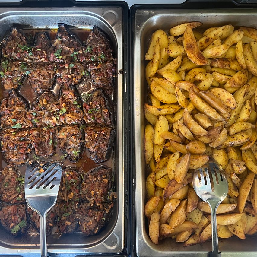 Zwei Tabletts halten ein Gericht aus Auberginen und Kartoffeln, jeweils mit Kräutern und Gewürzen gewürzt. Die Auberginen sind braun und ölig, während die Kartoffeln goldbraun sind.