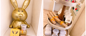 Eine goldene Hasenfigur steht neben einer Lebensmittelbox, mit anderen Kisten und einem Behälter in der Nähe. Ein dreistufiges Holzdisplay hält verschiedene Produkte, darunter Kisten mit orangefarbenen Bändern und einer gelben Kiste.
