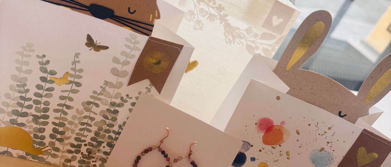 Handgefertigte Hasentüten und Grußkarten mit bunten Designs sind auf einem Tisch ausgestellt. Jede Tüte zeigt ein Hasengesicht und wird von passenden Karten begleitet. Accessoires wie Armbänder und Ohrringe sind ebenfalls vorhanden.