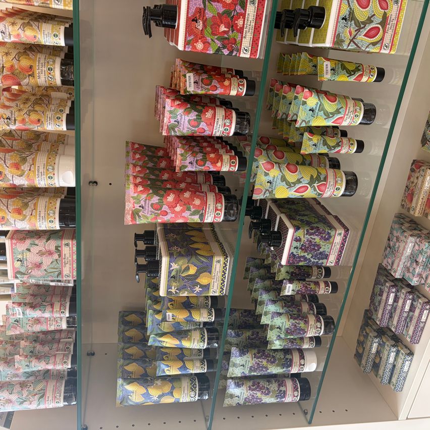 A glass shelf displays multiple rows of lotion tubes with various fruit designs and black pumps. The tubes have labels with small icons.