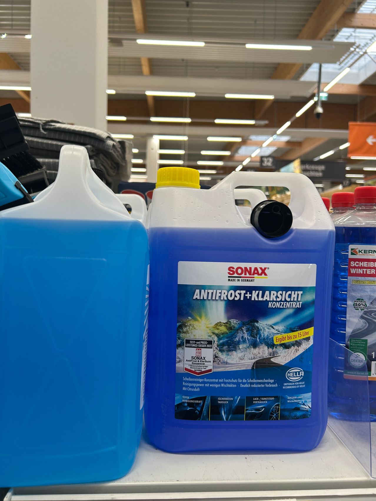 Eine große blaue Flasche Sonax Antifrost+Klarsicht Konzentrat wird in einem Geschäft ausgestellt, umgeben von anderen Flaschen und Produkten.