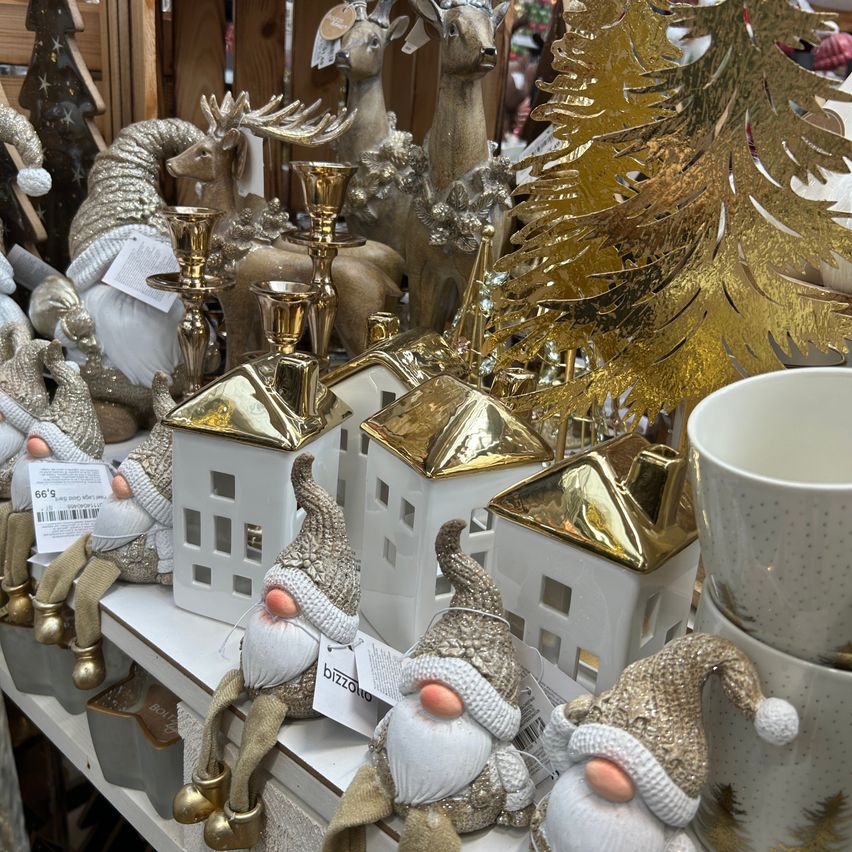 Eine Ausstellung von goldenen und silbernen Gnom-Figuren, Häusern und Dekorationsartikeln auf einem Regal mit goldenen Weihnachtsbäumen im Hintergrund.