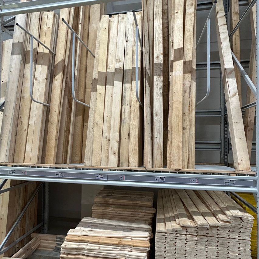 Ein Lagerraum gefüllt mit ordentlich gestapelten Holzbrettern auf Regalen. Die Bretter variieren in Größe und Dicke, einige stehen aufrecht, während andere horizontal verlegt sind.