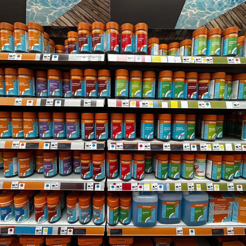 Ein Supermarktregal mit verschiedenen Marken von Poolreinigungsprodukten, einschließlich Tabletten und Flüssigkeiten, auf Regalen ausgestellt.
