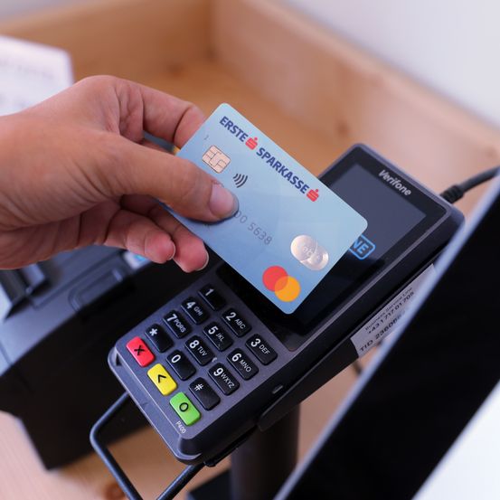 Eine Person hält eine blaue Kreditkarte von Erste Sparkasse mit einem Visa-Logo über einem Verifone-Zahlungsterminal.