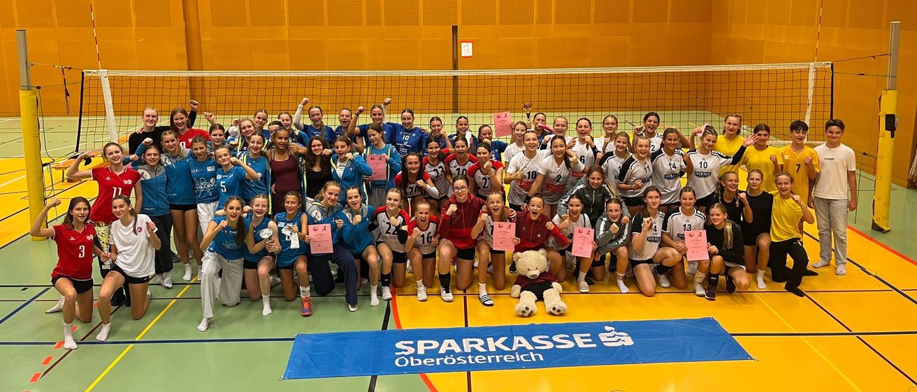 Eine Gruppe Volleyballspieler in einheitlichen Trikots posiert für ein Foto in einer Turnhalle, mit einem großen Banner, das Sparkasse Oberosterreich liest.