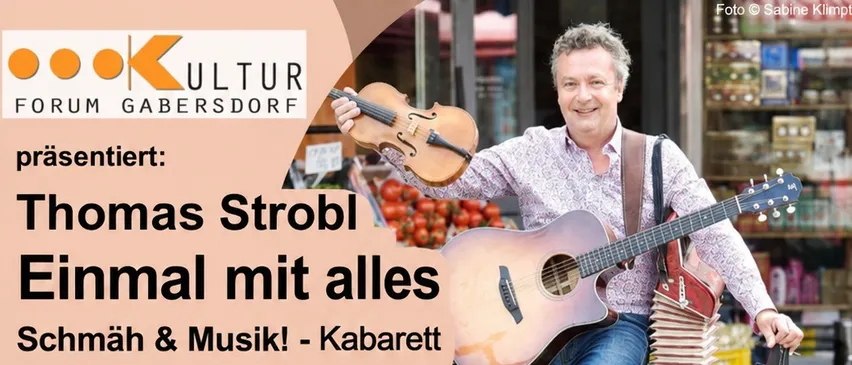 Ein Mann steht auf einem grünen Pfosten mit einer Geige und einer Gitarre in den Händen. Er lächelt und scheint für ein Foto zu posieren.