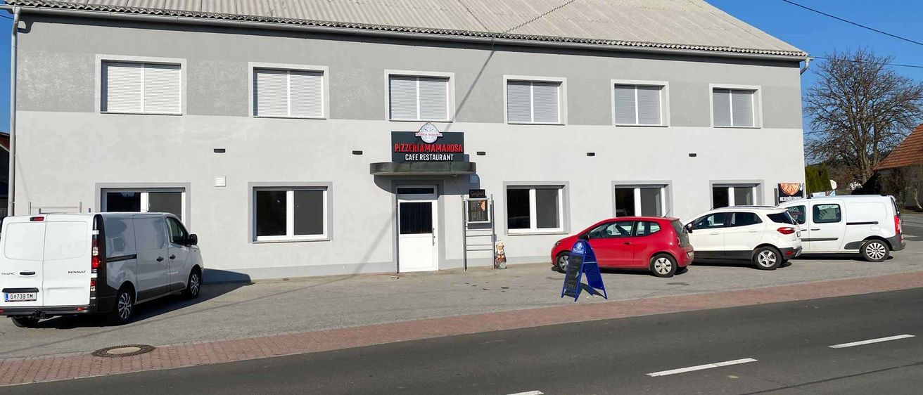 Ein graues Gebäude mit einem Schild, auf dem Pizzeria Mariposa Cafe Restaurant steht. Ein roter Wagen, ein weißer Wagen und ein Lieferwagen sind vor dem Gebäude geparkt.