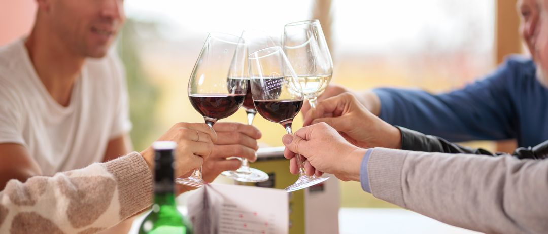 Eine Gruppe von Menschen prostet mit Weingläsern auf einem Tisch. Eine Flasche Wein steht in der Nähe.