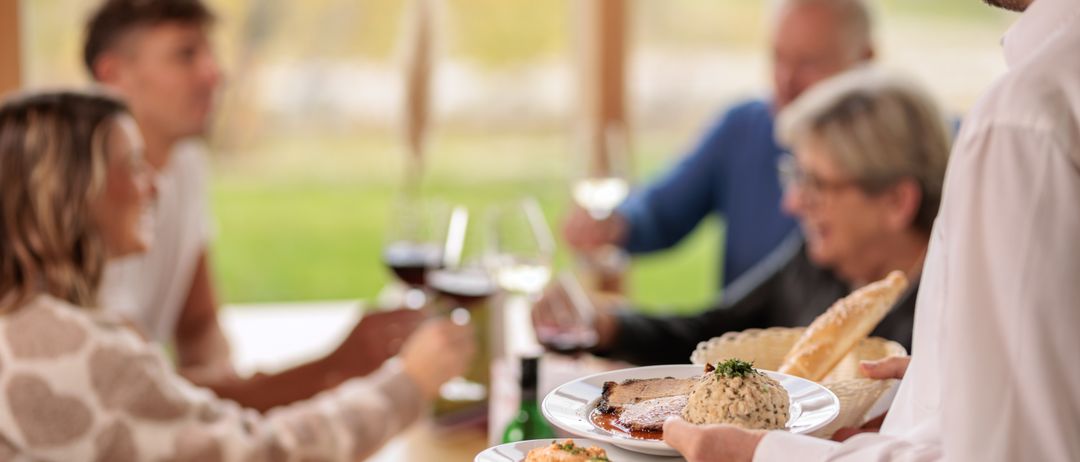 Eine Familie versammelt sich um einen Tisch und genießt eine Mahlzeit und Getränke. Teller mit Essen und Weingläser sind vorhanden.