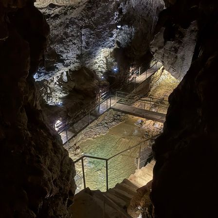 Ein Blick vom Eingang einer Höhle mit einer Metallbrücke über einem Wasserbecken und Treppen, die hinunter zum Becken führen.
