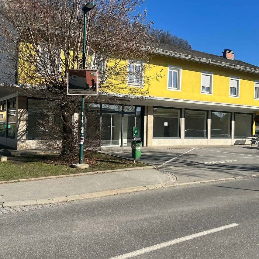 Ein gelbes Gebäude mit mehreren Fenstern steht neben einer Straße und bietet einen Parkplatz und einen Mülleimer in der Nähe eines Baumes.