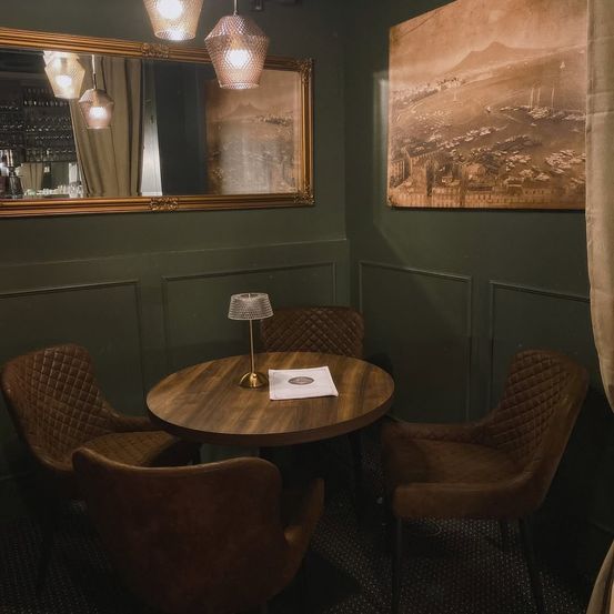 Ein kleiner runder Holztisch mit vier braunen Stühlen in einem Raum mit grüner Wand, Spiegel und großem Bilderrahmen.