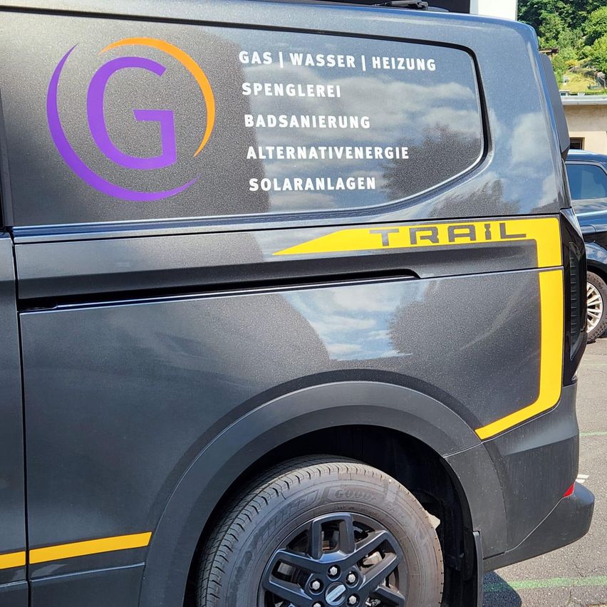 A black van with a yellow stripe and the word 'TRAIL' on the side. The van has a purple logo with the letter 'G' and some text written in white.