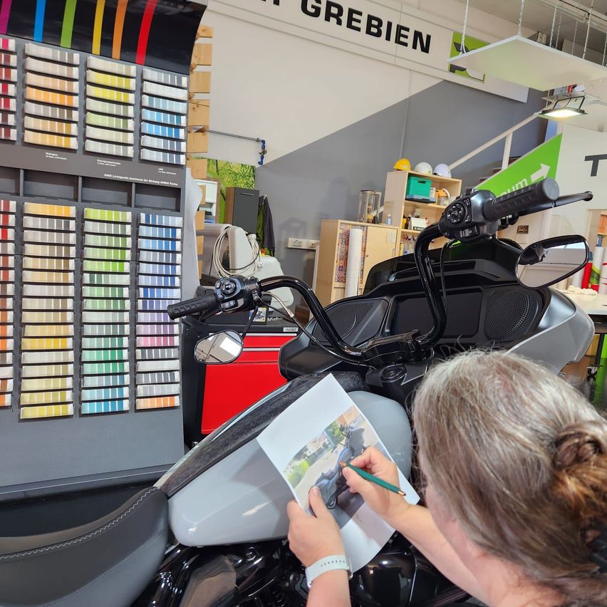 Eine Frau malt ein Motorrad in einem Geschäft mit einer Vielzahl von Farben an der Wand.